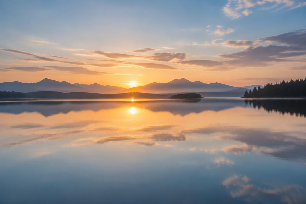 A calm, still body of water reflecting a soft sky at dawn